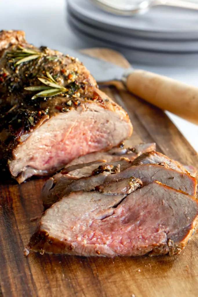Air fryer lamb roast on a wooden board with carving knife.