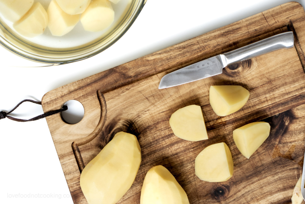 Peeled potatoes being cut on a wooden board.