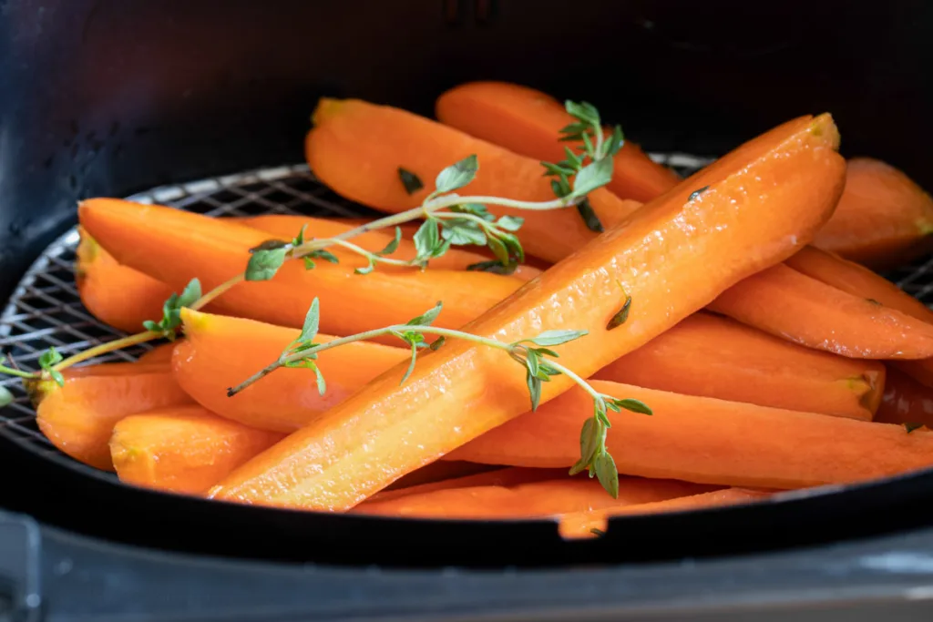 Raw carrots in air fryer basket. 