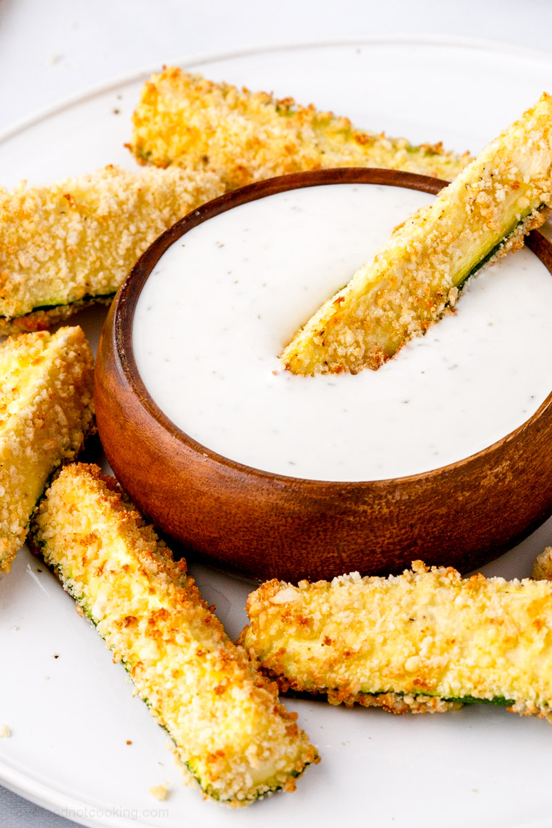 Air fried zucchini fries with dip on a white plate.