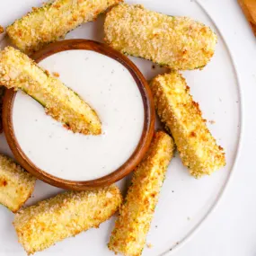 Air fryer zucchini fries with dip on a white plate.