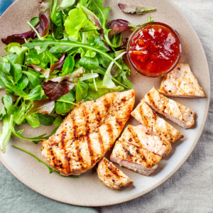 Pan seared chicken steaks on a grey plate with salad.