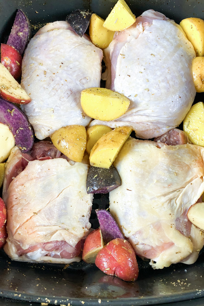 Uncooked bone-in chicken thighs in air fryer basket.