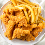 Air fryer dino nuggets and chips on a white plate.