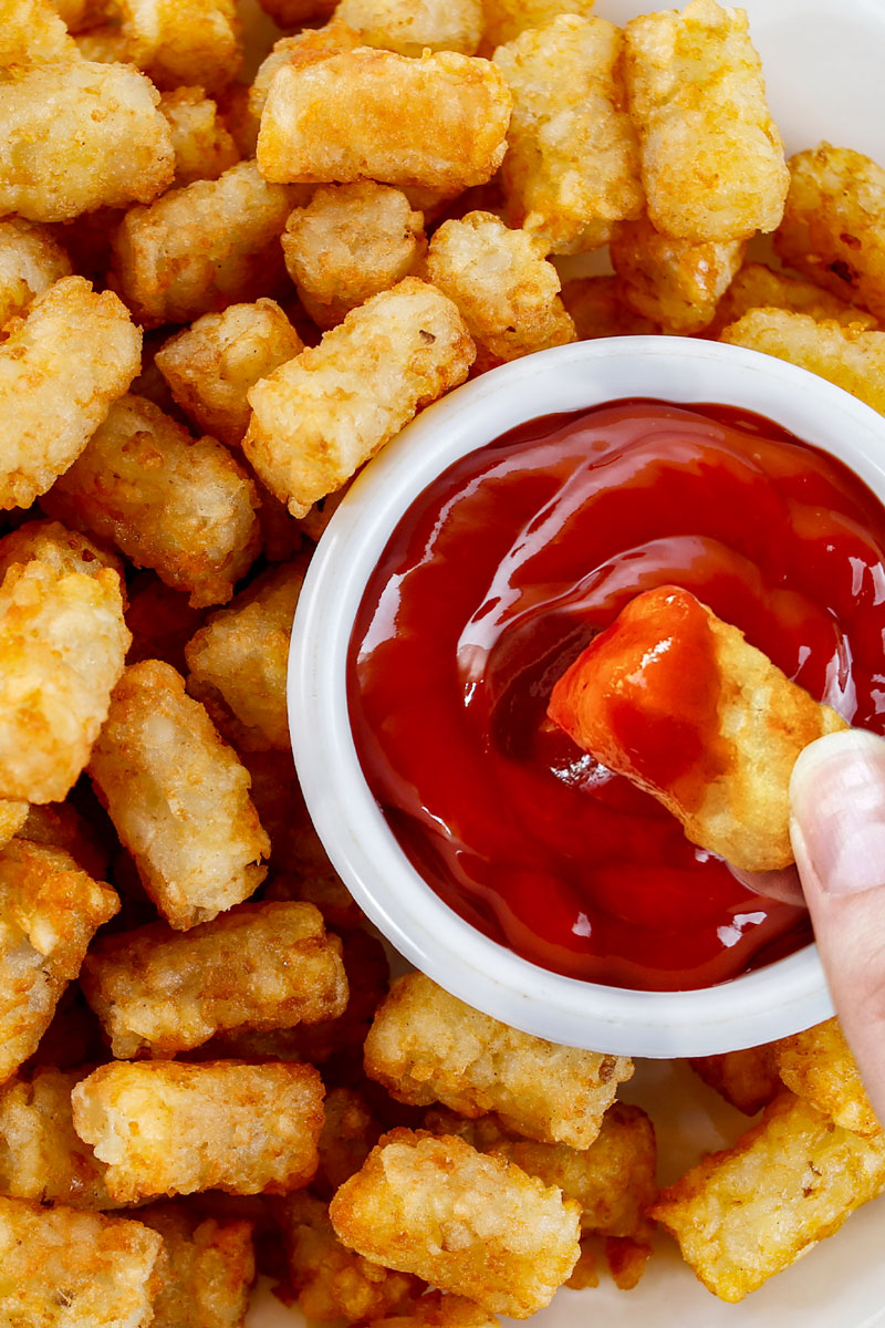 A hand dunks an air fried frozen tater tot into ketchup.