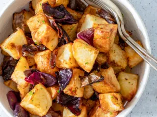 Air fryer potatoes and onions in a white bowl.