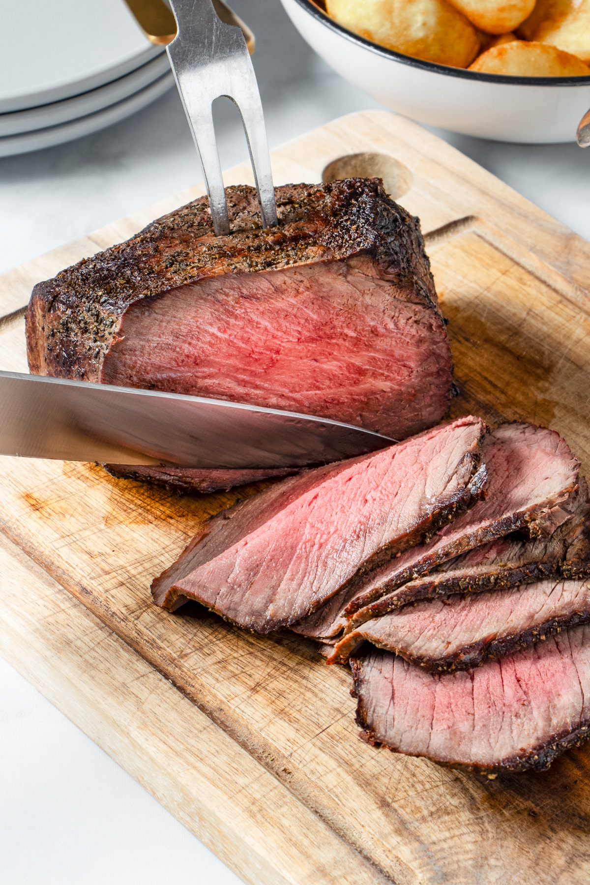 Air fryer roast beef joint being sliced on a wooden board.