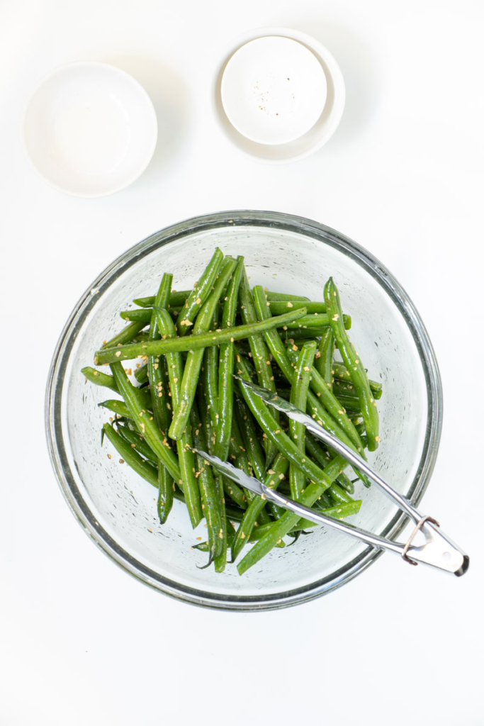 Green beans in a glass bowl with oil and seasoning. 