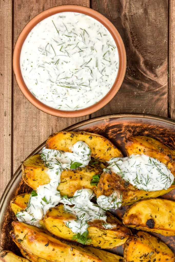 A bowl of dill mayonnaise and potato wedges drizzled with the sauce. 