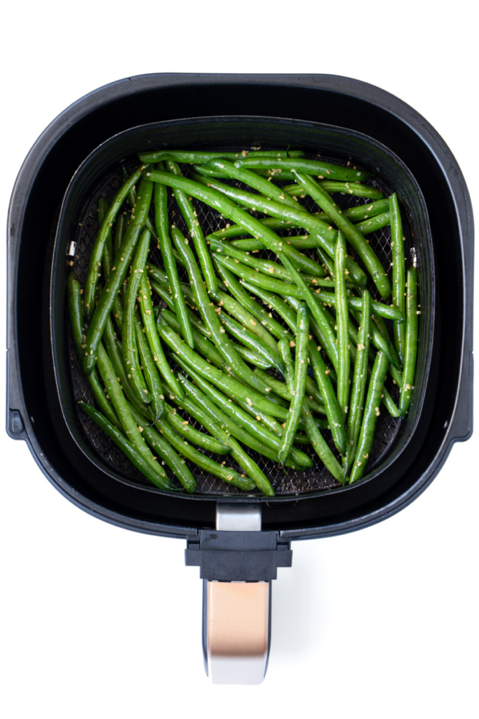 Green beans in air fryer basket, shows how they are spread evenly. 