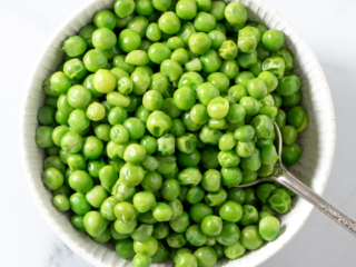 Microwave frozen peas in a white bowl.
