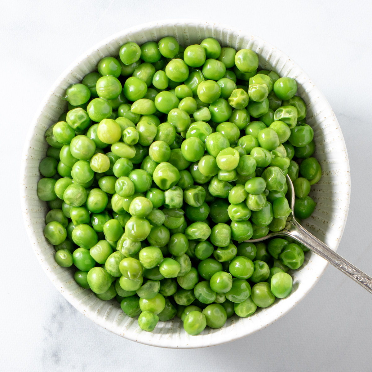 Microwave frozen peas in a white bowl. 