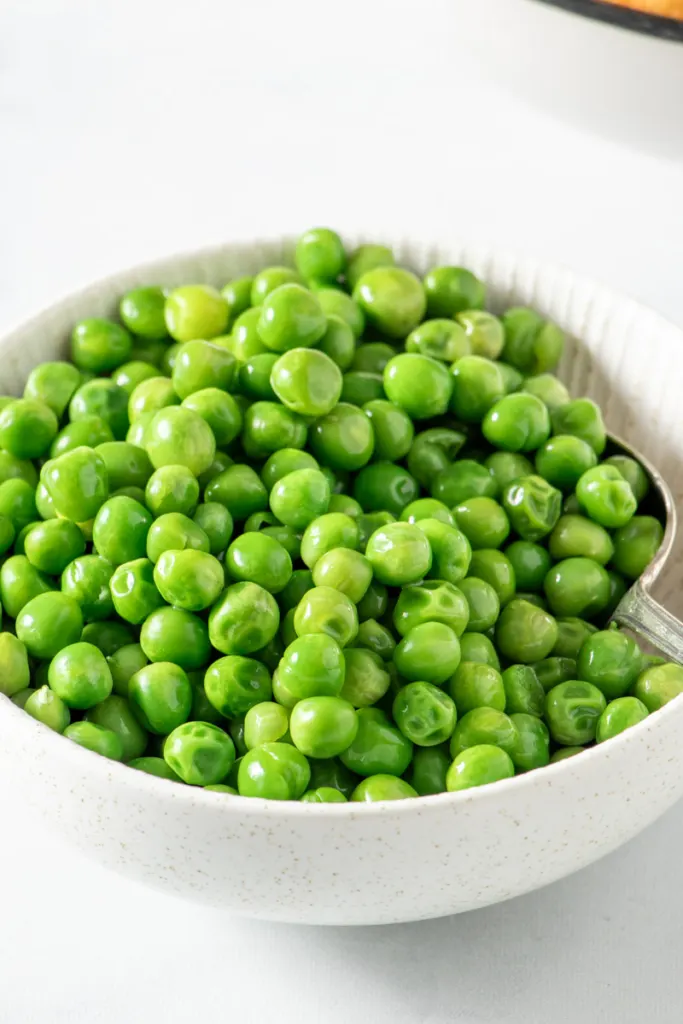 Microwaved frozen peas in a white bowl.