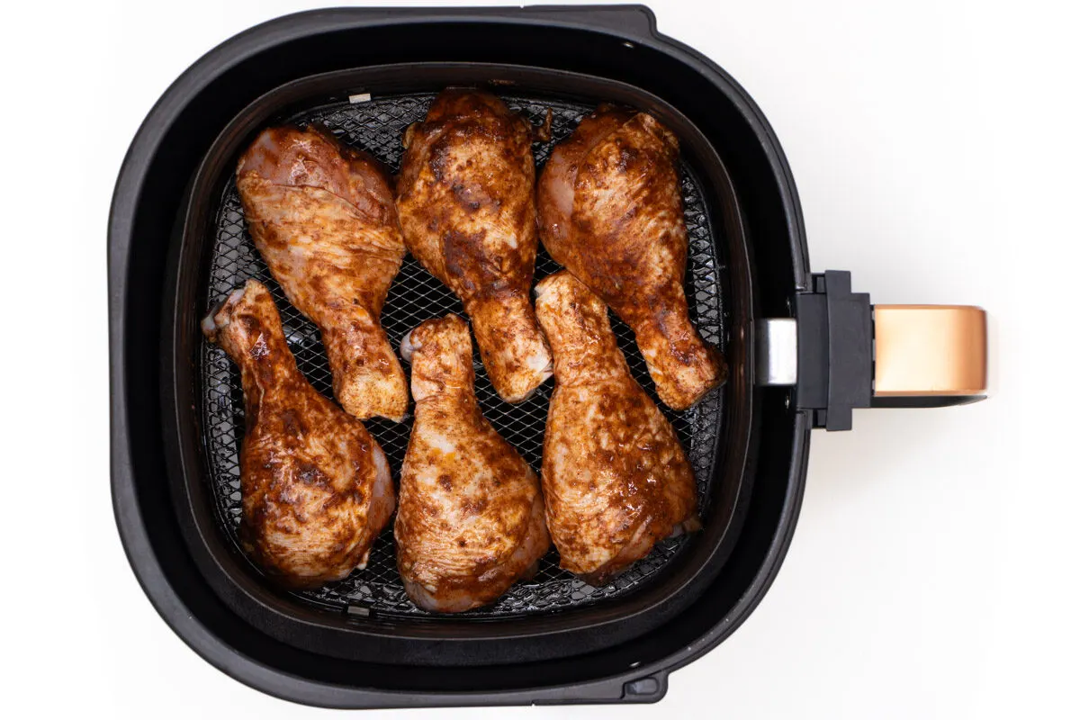 Uncooked chicken drumsticks in air fryer basket.