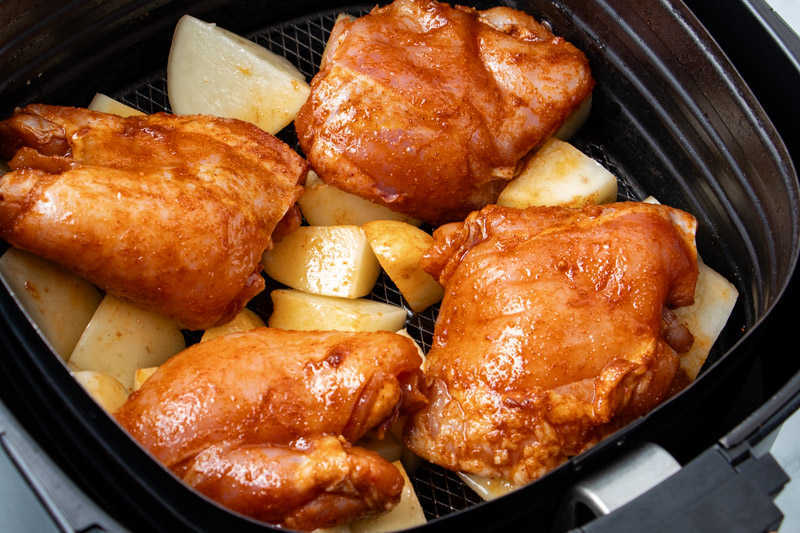 Uncooked chicken thighs and potatoes in air fryer basket. 