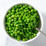 Microvaved frozen peas in a white bowl.