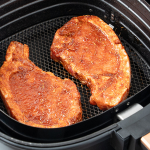 Uncooked pork chops in air fryer basket.