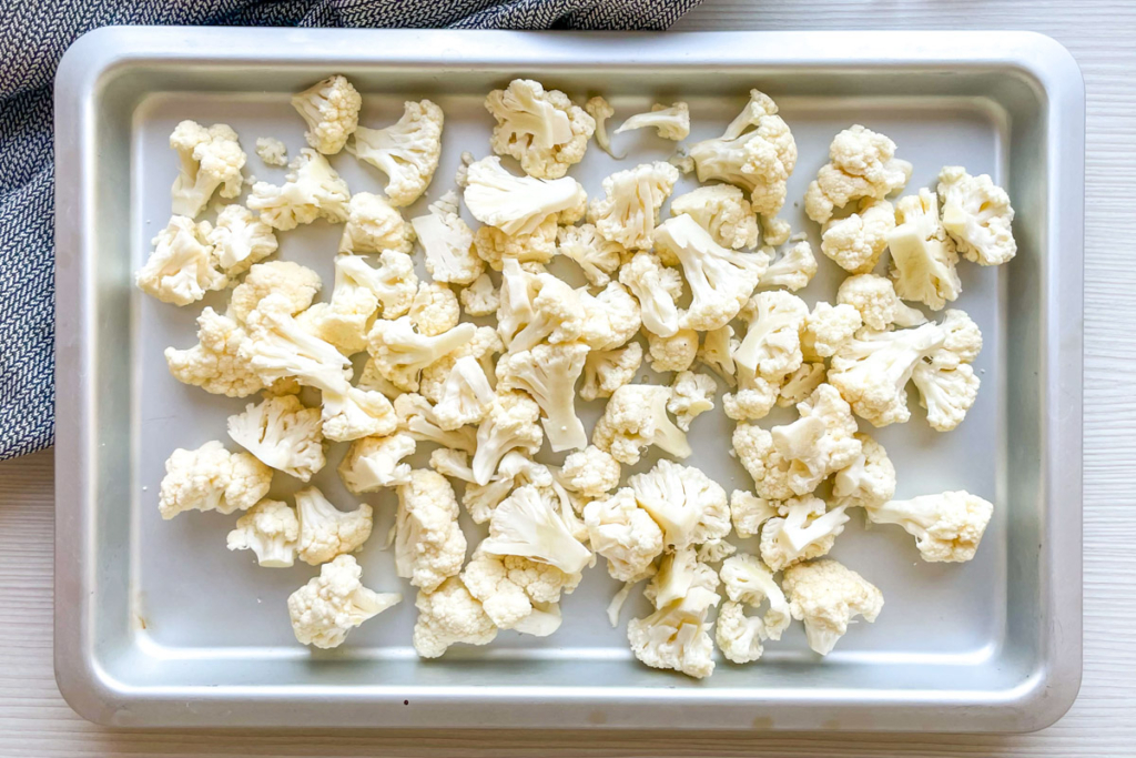 Raw cauliflower florets on baking sheet. 