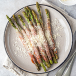 Air fryer bacon wrapped asparagus on a white plate with parmesan.