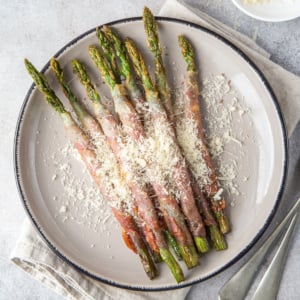 Air fryer bacon wrapped asparagus on a white plate with parmesan.