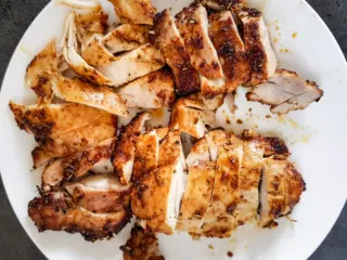 Sliced air fryer chicken thighs on a white plate.