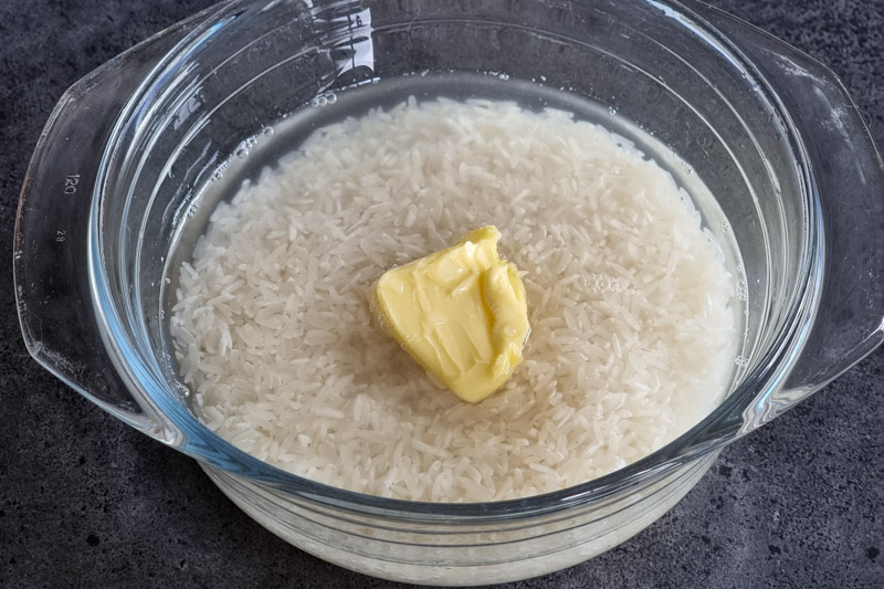 Rice, water, and butter in a glass baking dish.