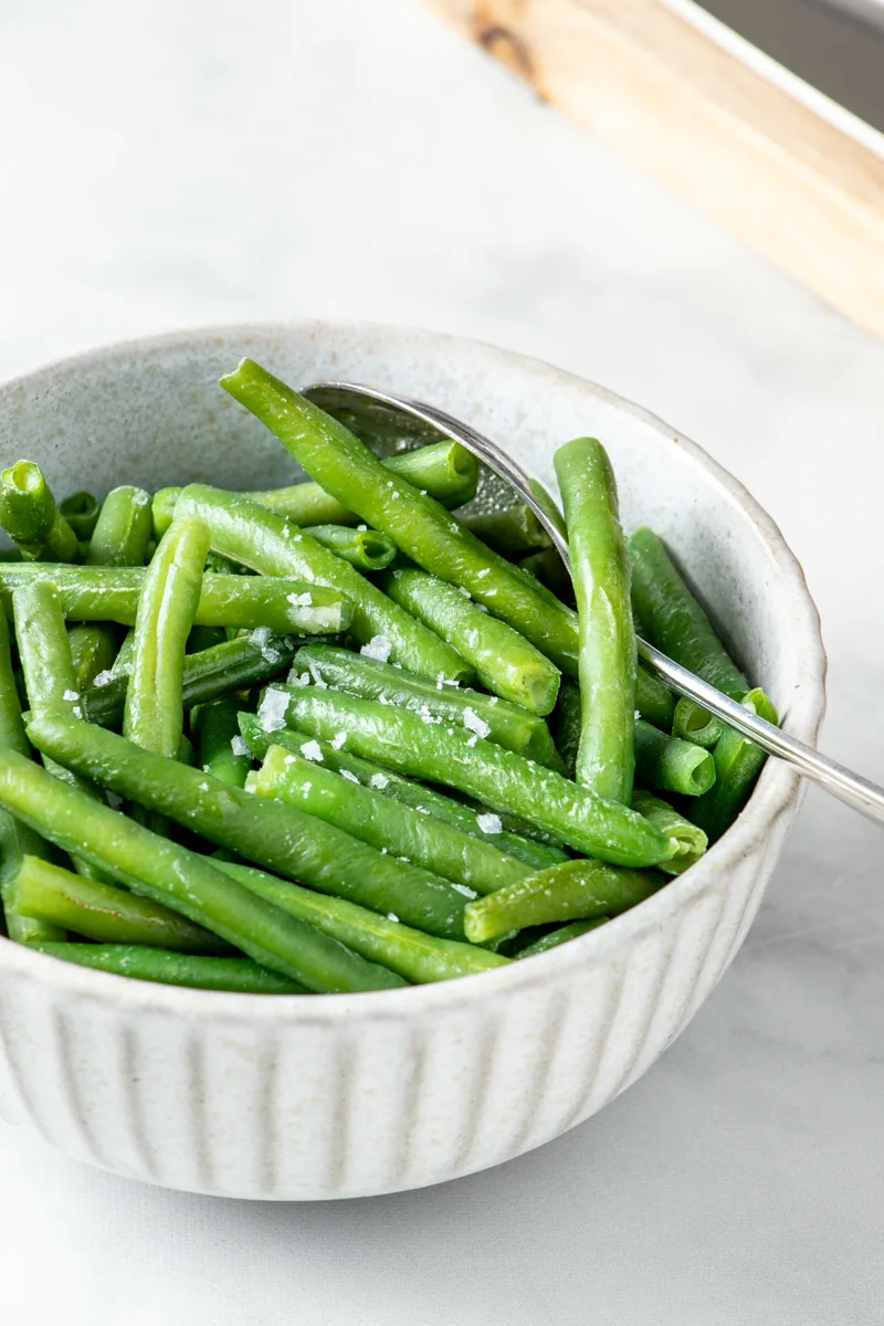 Microwaved frozen green beans in a white bowl. 