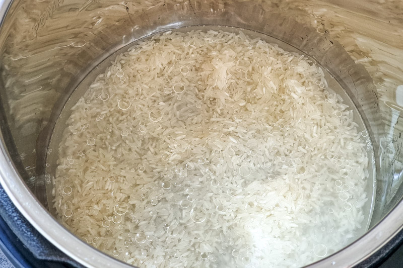 Uncooked jasmine rice and water in Instant Pot bowl.