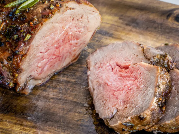 Sliced air fryer roast lamb on a wooden board.