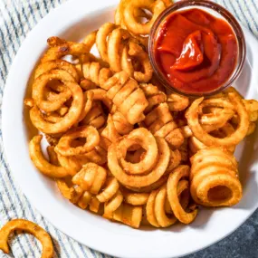 Air fryer curly fries in a white serving bowl with sauce.