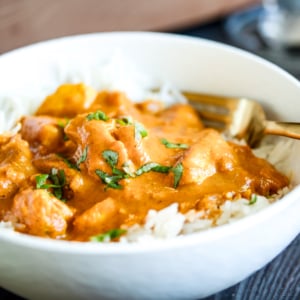 Butter chicken served over rice in a white bowl.