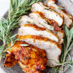Sliced air fryer roast turkey breast with fresh herbs on a plate.