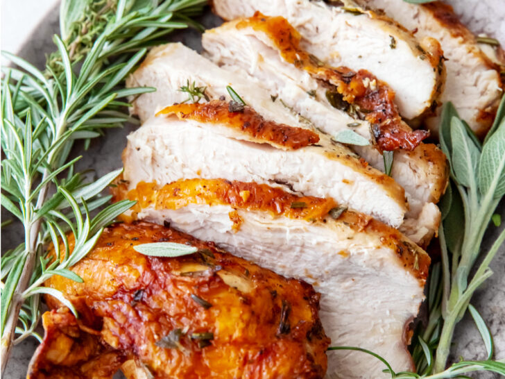 Sliced air fryer roast turkey breast with fresh herbs on a plate.