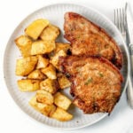 Crispy pork chop and potatoes on a white plate.
