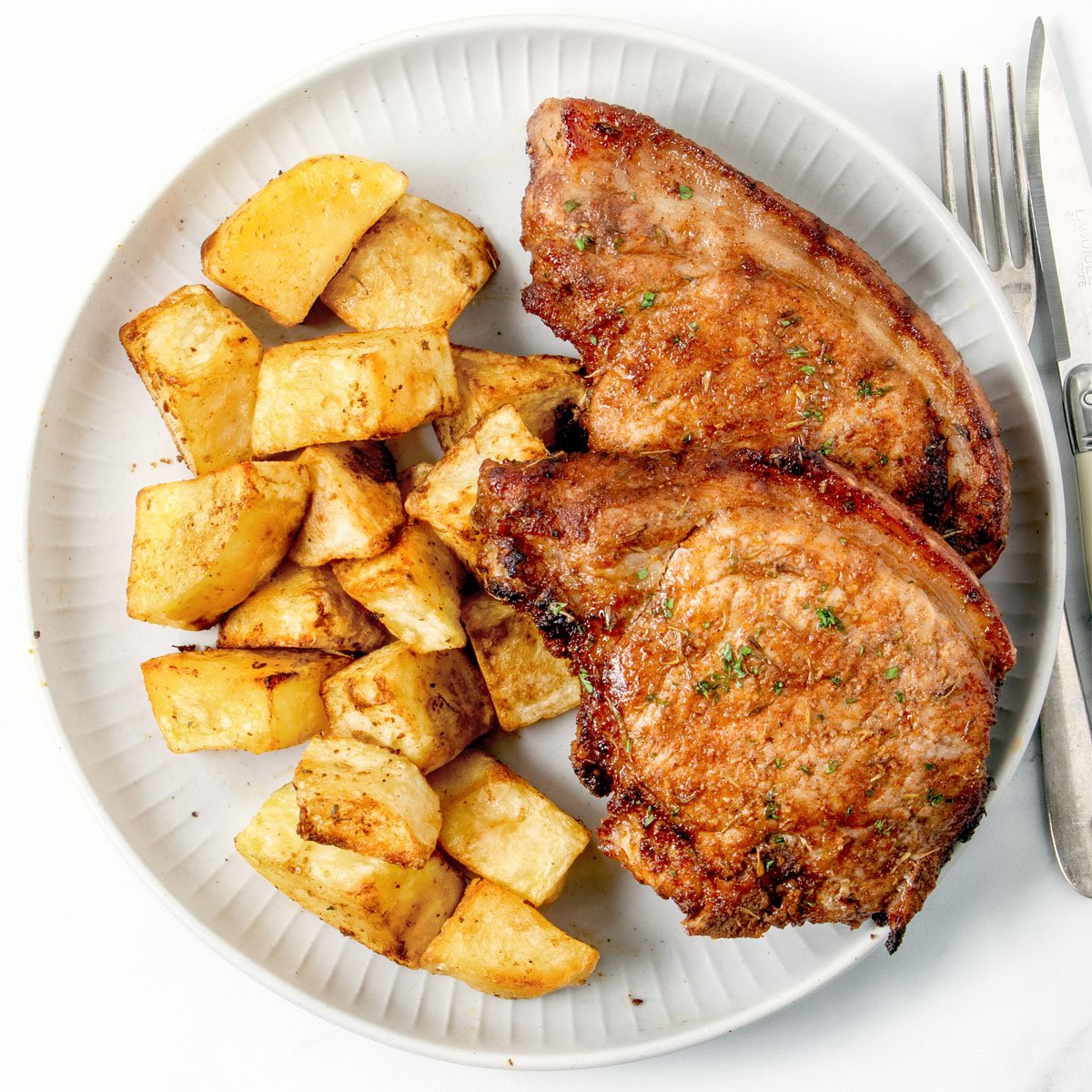 Crispy pork chop and potatoes on a white plate.
