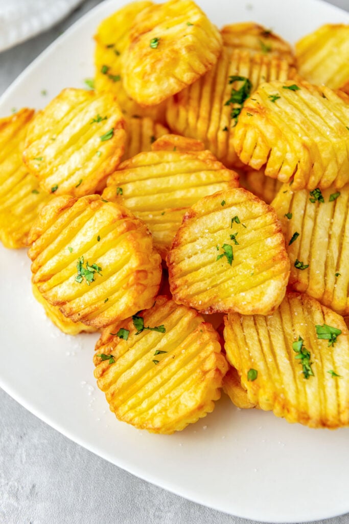 Golden air fried accordion potatoes on a white plate.