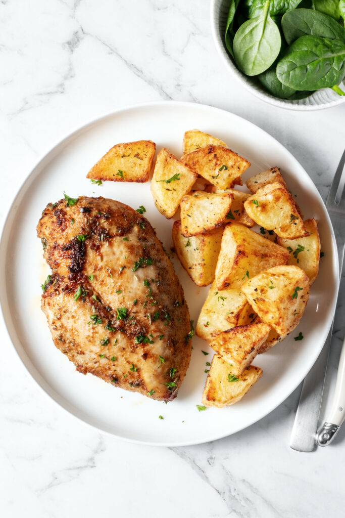 Air fried chicken breast and potatoes on a white plate.