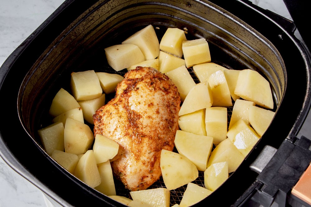 Chicken breast and potatoes in air fryer basket.