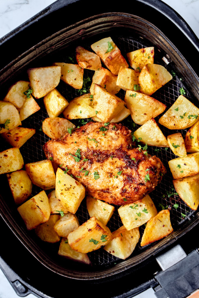 Chicken breast and potatoes in air fryer basket.