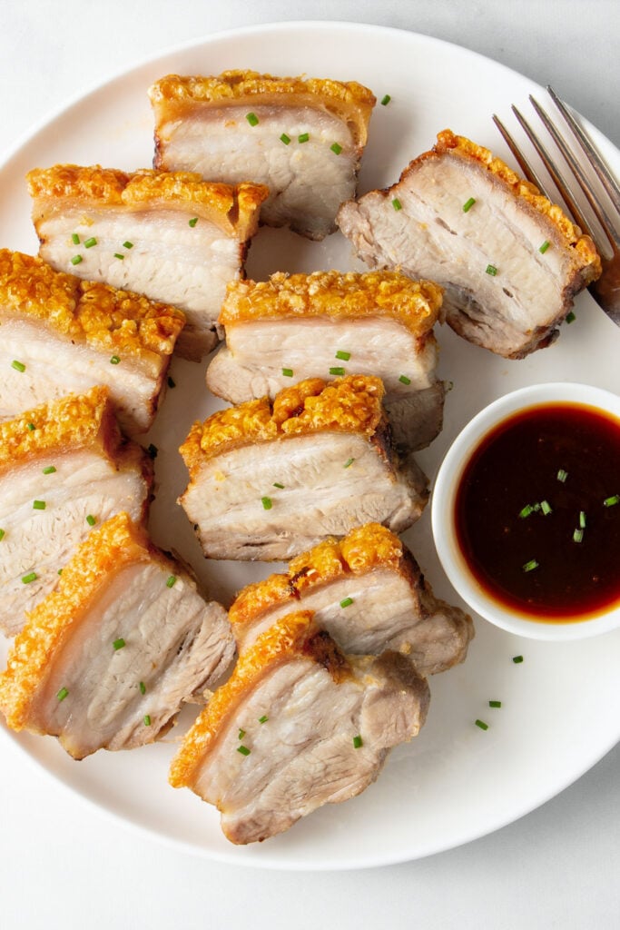 Slices of air fried pork belly on a white plate.