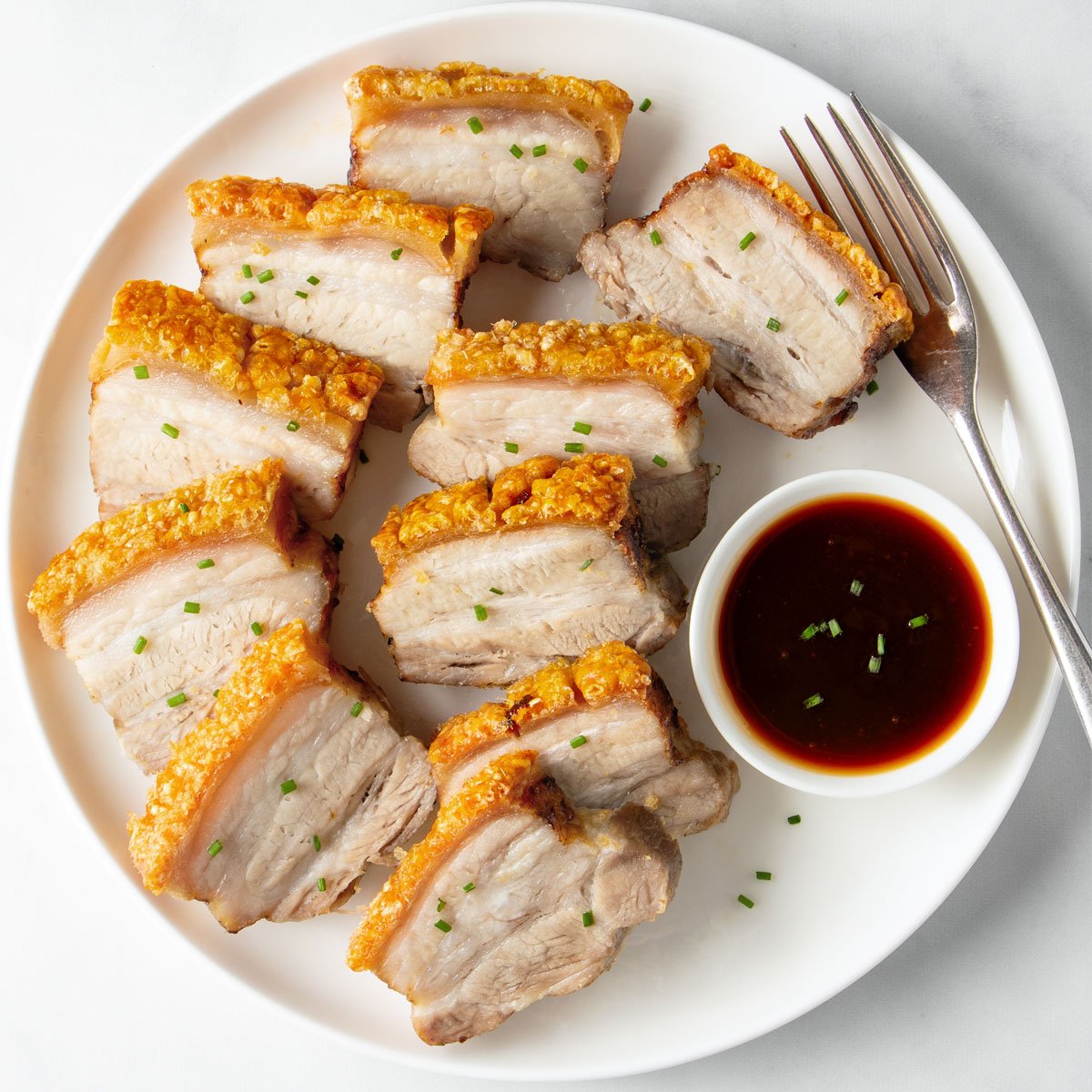 Sliced air fryer pork belly on a white plate.