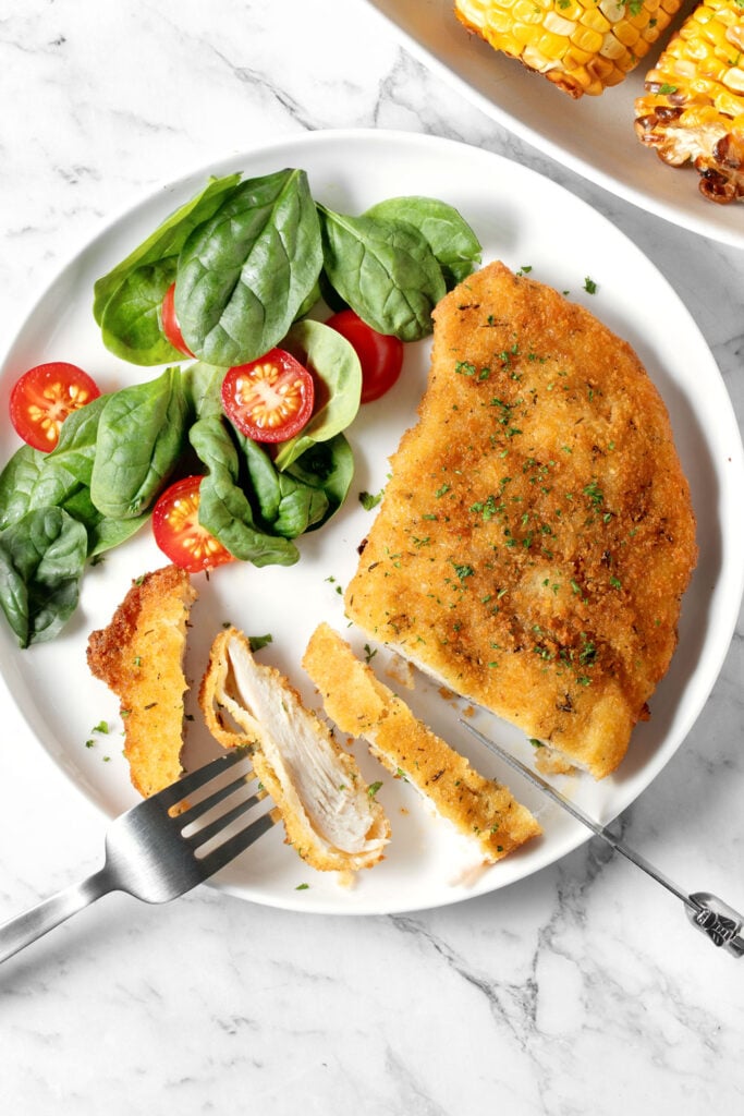 Air fried chicken schnitzel and salad on a white plate.