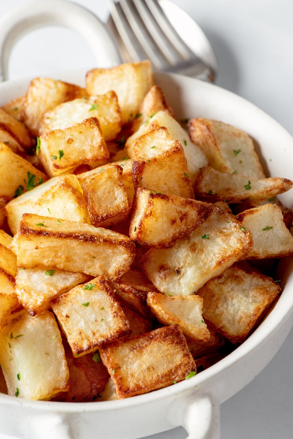 Crispy air fried potato cubes in a white bowl.