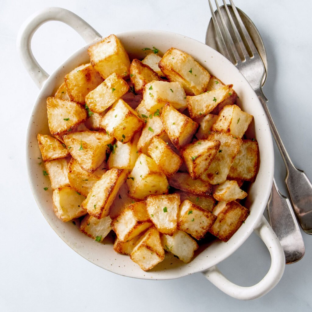 Crispy air fryer potato cubes in a white bowl.