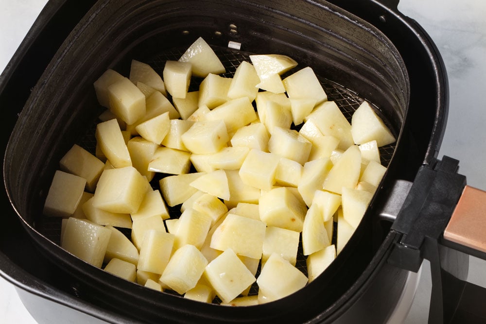 Uncooked potato cubes in air fryer basket.