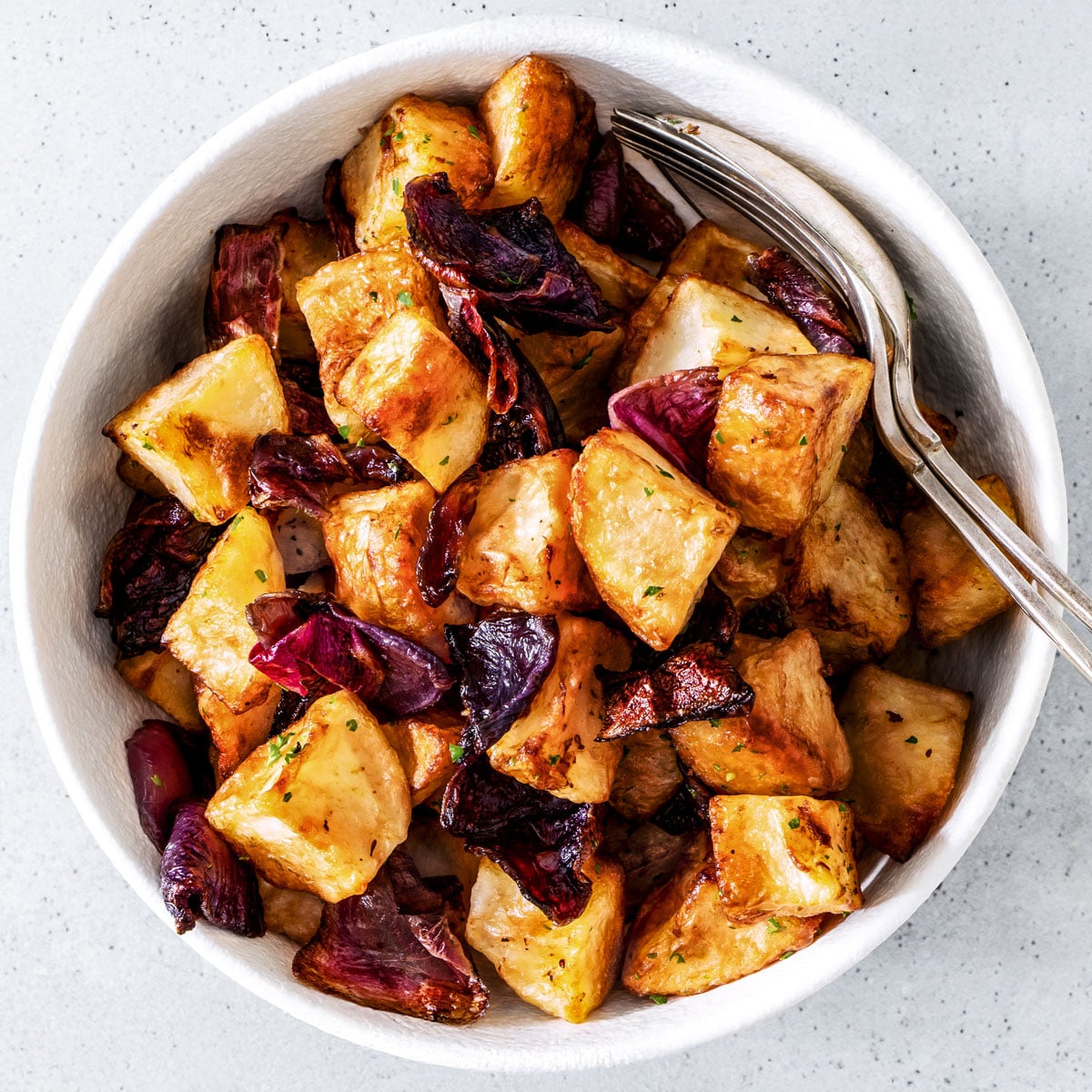 Air fryer potatoes and onions in a white bowl.