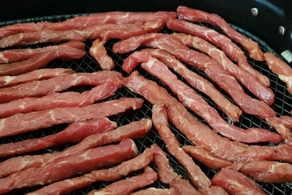 Strips of beef jerky in air fryer basket.