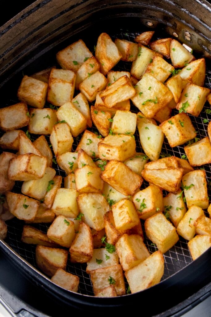 Crispy potato cubes in air fryer basket.