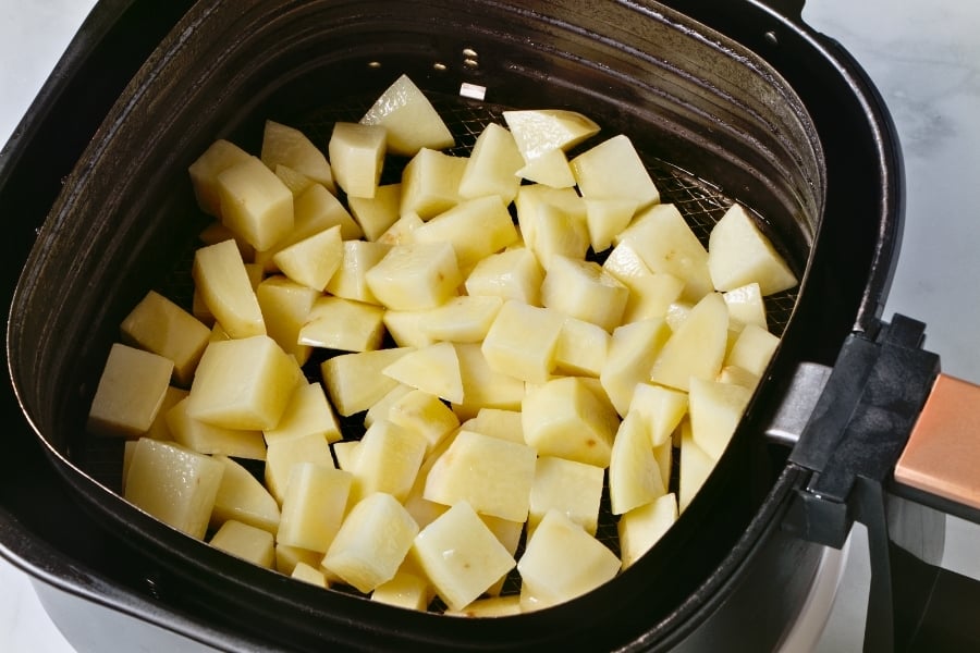 Uncooked potato cubes in air fryer basket.