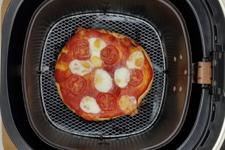 Cooked flatbread piiza in air fryer basket.